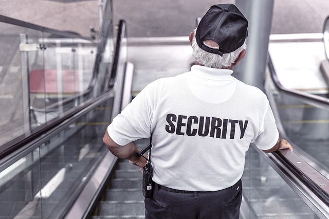 A photograph of a man in a uniform with the word "SECURITY" printed on the pack of his shirt